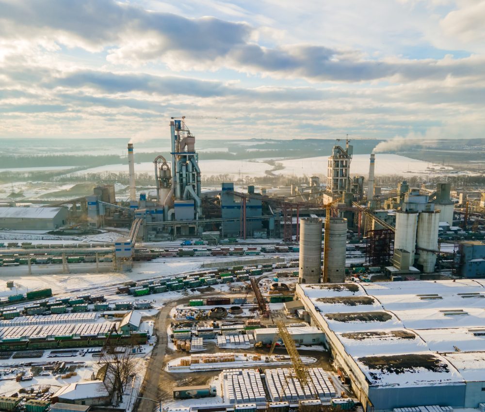 Aerial view of cement plant with high factory structure and tower crane at industrial production area.